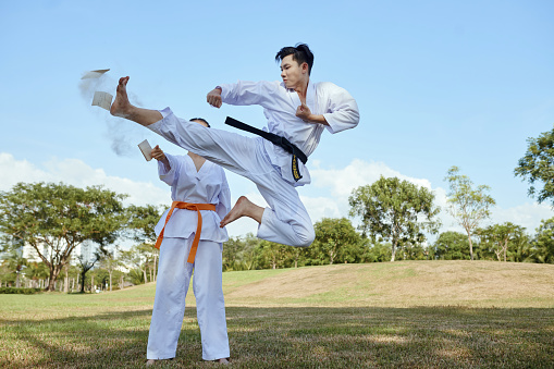 Taekwondo black belt athlete jumping and kicking wooden board to break