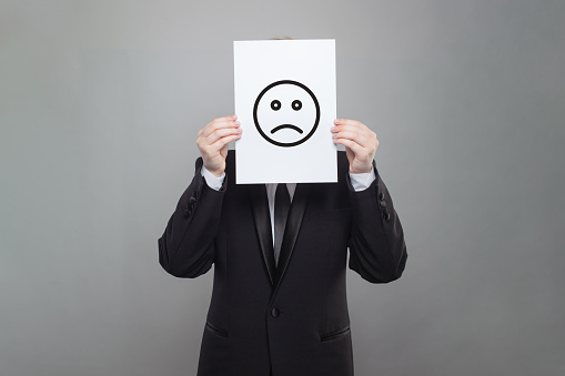 Sad emoticon on business person head on gray studio wall background