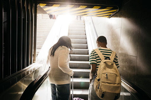 Rear view of a young female couple getting off the the metro throught the escalators and reaching for the first time in a new city.