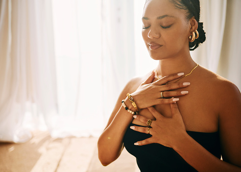 a woman deep in meditation, her hands placed gently on her chest as she focuses on her breath with her eyes closed. This moment reflects inner peace and mindfulness.