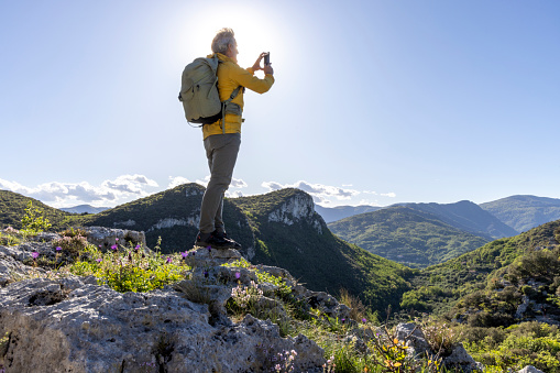 Senior hiker takes photo on mountain top and looks out over valley