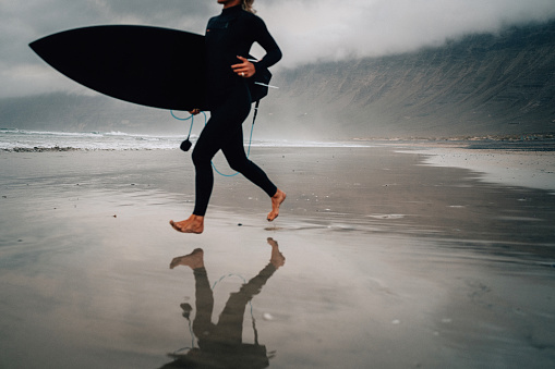 Surfer woman running with surfboard in Lanzarote Canary Islands, Famara beach