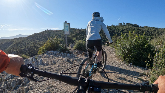 POV past handlebars to young woman e-biking to coastal viewpoint
