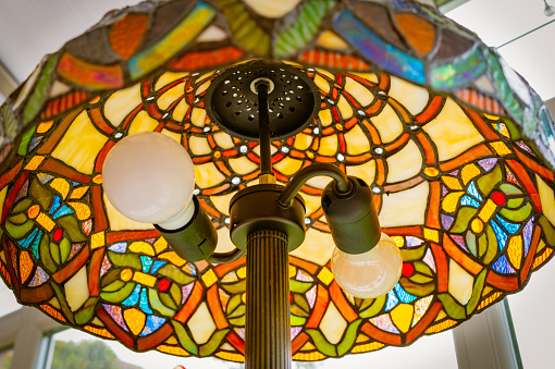 Unusual, vertical aspect of a large, hand made glass Tiffany lamp showing the double light holders. The colourful, ornate design is clearly visible.