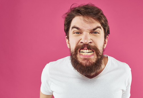 An angry man with a bushy beard bared his teeth against a pink background. High quality photo