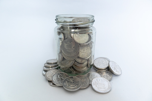 Indonesian Rupiah coins in glass jar and scattered coins with white background