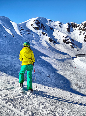 A skier in vibrant gear stands against a stunning backdrop of pristine snow-covered slopes and a clear blue sky, poised for an exhilarating descent.