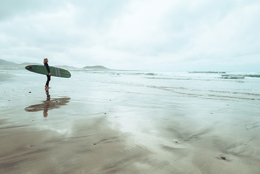 Surfer woman with longboard surfboard at Famara beach in Lanzarote Canary Islands