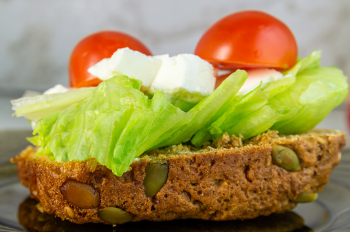A sandwich with lettuce and tomatoes on a plate. The sandwich is made of bread and has a crunchy texture. The lettuce and tomatoes are fresh and colorful, giving the sandwich a healthy