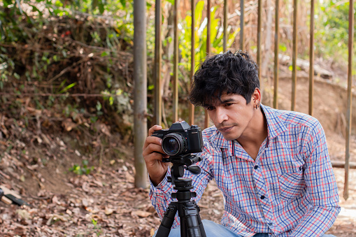 outdoor lifestyle concept. Young Latino photographer using camera on tripod.