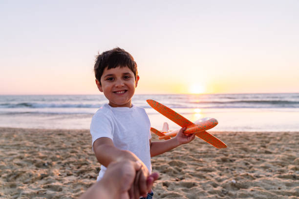 istock Cheerful Boy Offering Foam Airplane on Sunset Beach 2149840060