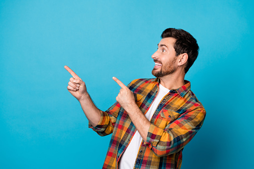 Portrait of eccentric guy with stubble wear checkered shirt look indicating at awesome offer empty space isolated on blue color background.