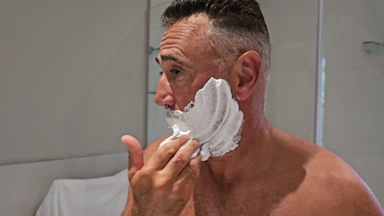 Face of man applying foam on his chin with concentration