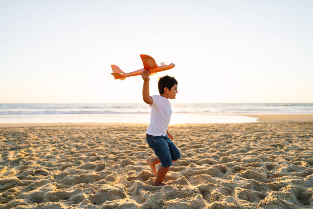 istock Boy Running with Bright Toy Plane on Sunny Beach at Dusk 2149840603
