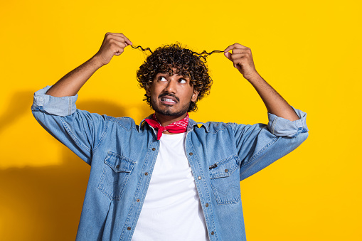 Photo portrait of handsome young guy look worried curly strands dressed stylish jeans garment red scarf isolated on yellow color background.
