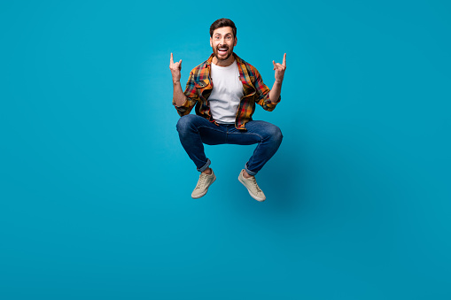 Full length photo of nice young guy jumping excited rocker wear trendy plaid garment isolated on blue color background.