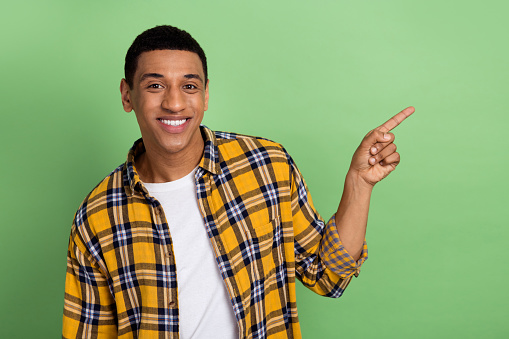 Portrait of nice positive man toothy smile indicate finger empty space ad isolated on green color background.