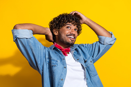 Photo portrait of nice young male touch hair look empty space dressed stylish denim outfit red scarf isolated on yellow color background.