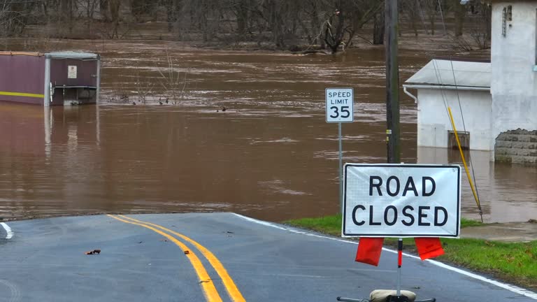 Road closed sign with brown, murky flooded water on riverbed and street. Aerial of natural disaster.