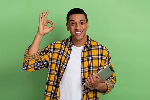 Portrait of handsome guy hold tablet hand fingers demonstrate okey symbol isolated on green color background.