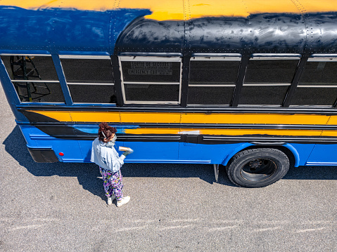Smiling preteen boy getting of the yellow school bus, cheerful male kid wearing backpack stepping down off of the vehicle as he arrives for study, ready for lessons and learning fun, free space
