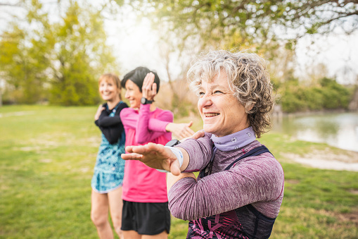 Joyful senior stretching, women sharing a light-hearted moment during a fitness routine in the park. Healthy lifestyle concept for mature women