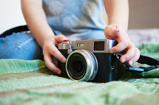 Close up of a mirrorless retro camera on the bed. Little girl playing with camera. Talented little girl has fun with vintage camera at home. Leisure activity at home. Young female talent with tech.