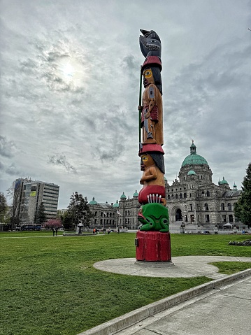 The Knowledge Totem standing in front of the British Columbia legislature in Victoria, BC, Canada. The sun shinning through the clouds. Legislative Assembly