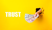 A hand holding a stack of money with the word trust written below it