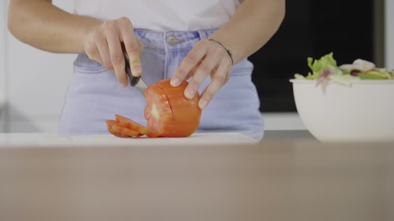 Home chef slices juicy ripe tomato salad in bright kitchen scene slow motion mid shot