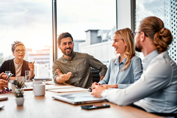 istock Four business people sitting along table while communicating and laughing in office space. 2149849486