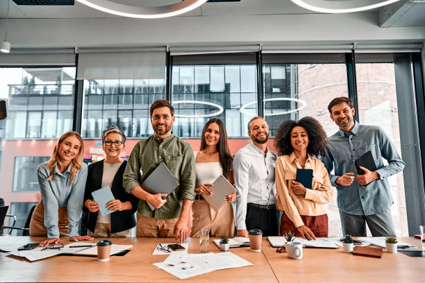 istock Beginning of working day in office. Diverse people gathering at common space and smiling at camera with tablets and laptops in hands. 2149850720