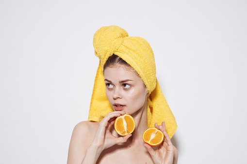 Cheerful woman with a yellow towel on her head bared shoulders oranges in hands health clean skin. High quality photo