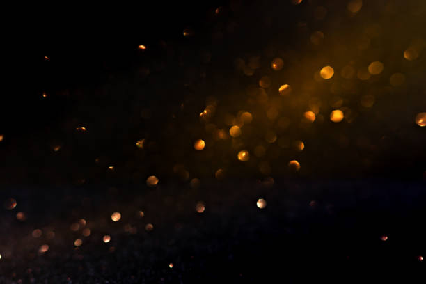 Warm golden bokeh lights illuminate a dark backdrop, creating an abstract pattern of soft glowing orbs ideal for backgrounds. Blurred shine bokeh for overlay effect.