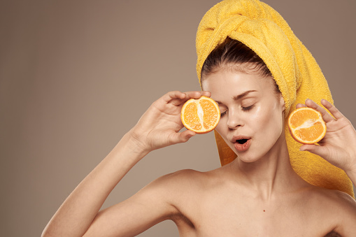 woman with a towel on her head bared shoulders citrus fruits in hands skin care. High quality photo