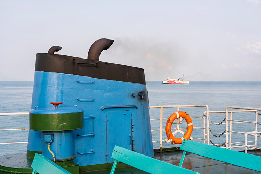 Smoke from ferry boat flue during sea with sunlight, sea water and blue sky in background, Thailand. Aboard, chimney of a ferry or cruise ship, smokestack pollutes the atmosphere