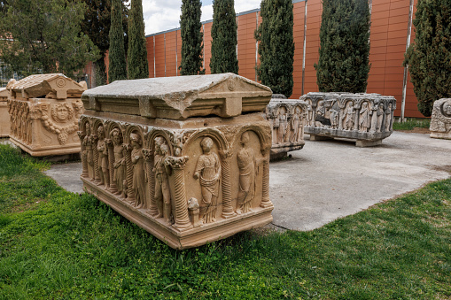 Well-preserved sarcophagi with bas-relief figures in the historic site of Aphrodisias, set against a backdrop of greenery.