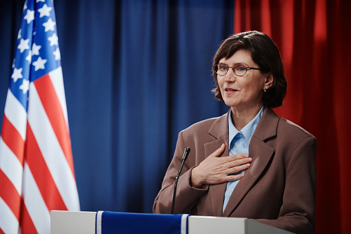 Mature female candidate for president post keeping hand on chest and looking at electorate while speaking in microphone