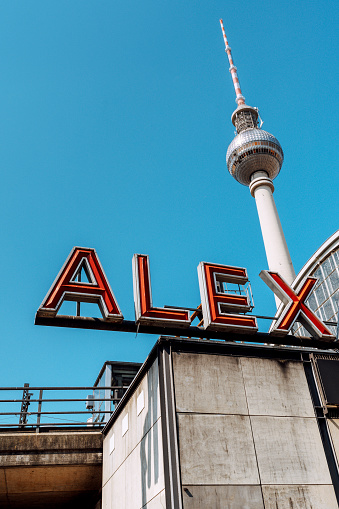 Striking view of Berlin's famous TV Tower and the bold Alexanderplatz sign against a clear blue sky. Captured in Berlin, Germany, showcasing urban architecture and historical landmarks.