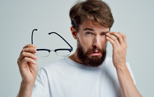 a man with narrowed eyes holds glasses in his hand on a light background vision problems. High quality photo