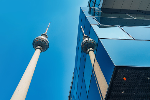 Architectural perspective in Berlin, capturing the iconic TV Tower beside a modern glass building against a clear blue sky.