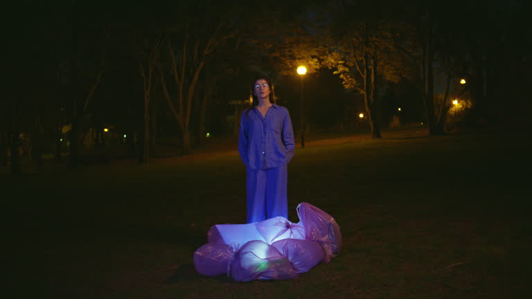 Pensive girl standing night park with lantern light under glowing waste bags