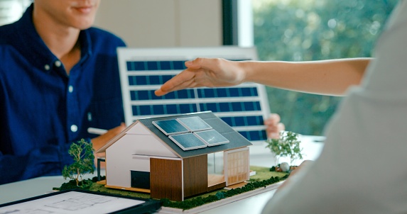 Closeup of young Asian couple in detailed consultation with real estate agent, who is highlighting advantages of home with solar panels. Consulting on Eco-Friendly Home with Real Estate Agent Concept.