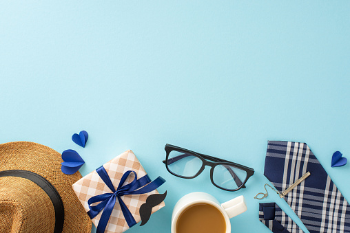 Send warm wishes to Dad with a charming top view scene including a straw hat, stylish necktie, gift box with ribbon, eyeglasses, mustache props, coffee cup on soft blue backdrop, ideal for adverts