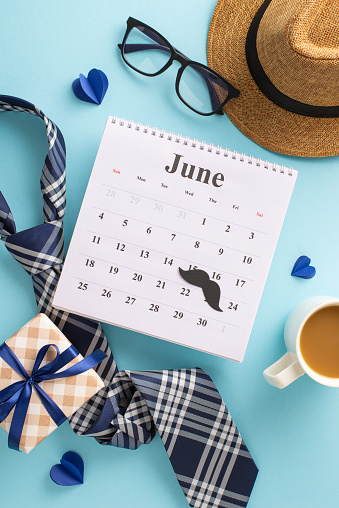 Pay tribute to Dad on Father's Day with a delightful vertical ensemble comprising top view of June calendar, hat, refined necktie, mustache, ribbon-wrapped gift box, and more on soft blue background