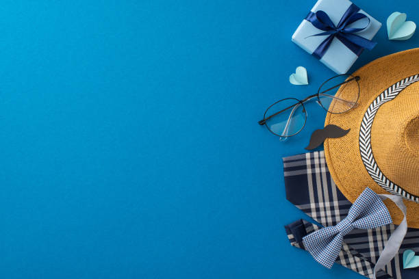 istock Top view arrangement for Fathers' Day featuring straw hat, necktie, bow tie, giftbox, glasses, mustache props, and hearts on blue surface. Space reserved for personalized greetings or promotional text 2149858792