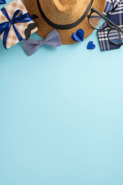 istock Father's Day celebration vertical setup featuring a straw hat, eyeglasses, gift box, bow tie, and paper hearts on a light blue background 2149858796
