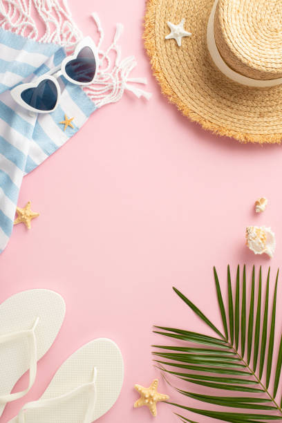 istock Vertical overhead view of summer holiday accessories spread out on a pink surface. The image features a straw hat, sunglasses, flip-flops, a beach towel, seashells, and a palm leaf 2149858806