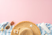 Top view of a straw hat, stylish sunglasses, starfish, and sunscreen, neatly laid out on a striped cloth against a soft pink background. Perfect depiction of beach vacation and summer holidays