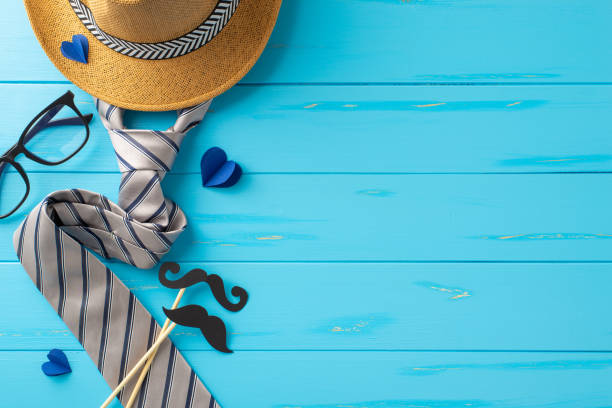 istock Creative and stylish Father's Day setup featuring a straw hat, elegant necktie, glasses, and playful mustache cutout on a blue wooden background 2149858813
